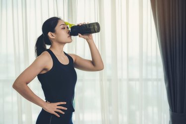 一个女人拿着一瓶蛋白质补充剂对肌肉喝加强卫生保健激烈的和美丽的。