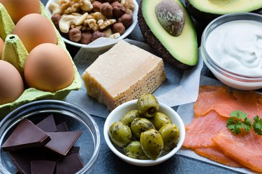 Selection of foods High in Healthy Fats such as olives, eggs, chocolate, salmon, yogurt