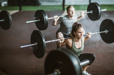 Young athletes exercising strength with barbells on cross training in a gym.