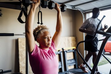 African American senior couple lifting weights and running on treadmill in their garage