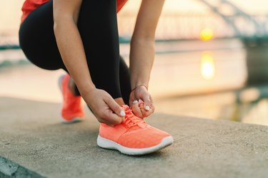 Close up of a person tying an orange sneaker, to illustrate wearing shoes that fit well to prevent ingrowns