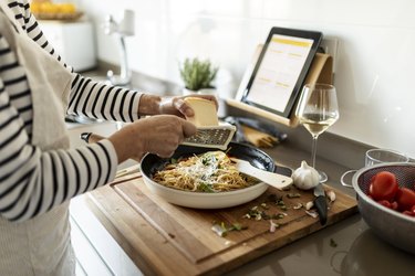 Close-up of woman with grating parmesan cheese on tomato pasta dish in her kitchen