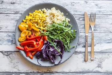 Glass of rainbow salad with bulgur, rocket and different vegetables and bowls with ingredients