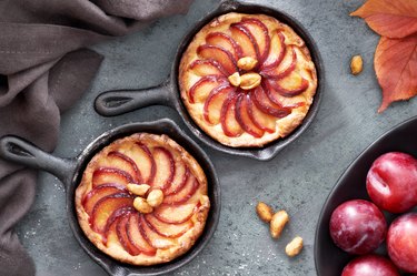 Homemade crumble tarts with plum slices baked in small iron skillets