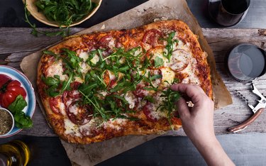 Preparing gourmet pizza, close-up of hand topping pizza with arugula