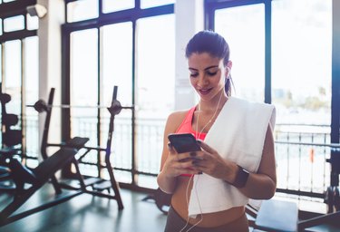 Woman using fitness application with smartwatch and smartphone at gym