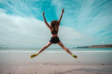 Young woman doing star jumps on the beach