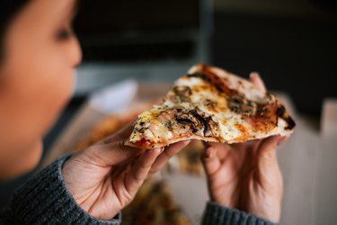 Woman holding slice of pizza, which is not a good food for height growth hormone