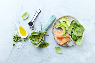 Ingredients for a healthy salad on gray stone background. Smoked salmon, avocado, spinach, sorrel, radis sprouts, black cumin. Flat lay. Healthy diet. Symbolic image.