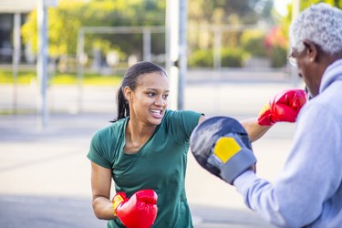 Young woman practicing boxing for health benefits outside with older man