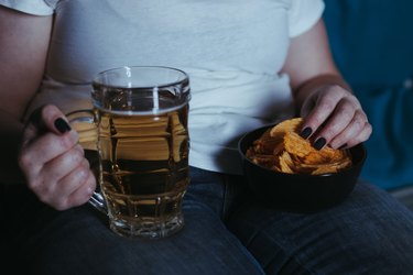 Woman watching tv eating junk food and beer