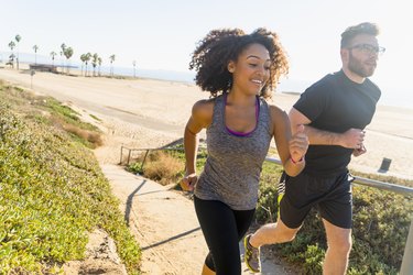 Couple runnExertion Headaches: A Pain, but Probably Not Dangerousing along pathway by beach