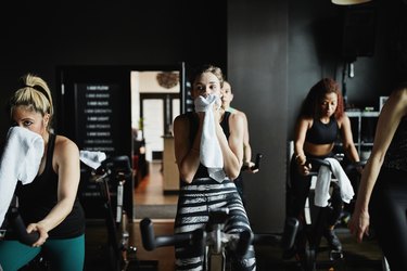 Woman wiping sweat from face with towel during indoor cycling class in fitness studio