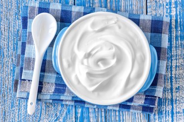 Sour cream in white bowl with spoon on blue background