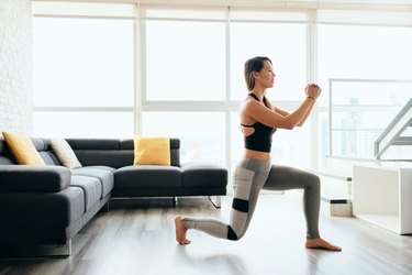 woman wearing leggings and tank top doing lunges in her living room