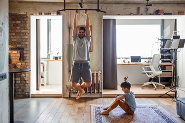 dad doing pull-ups at home while his son plays nearby