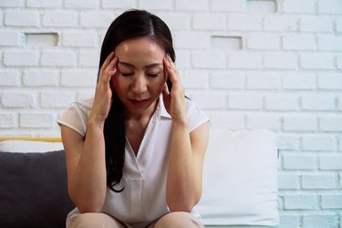 Beautiful stressed woman sitting with closed eyes and hands on head and suffering from headache at home