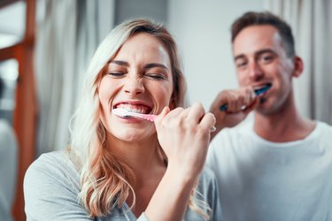 A woman and man brushing their teeth in the bathroom at home