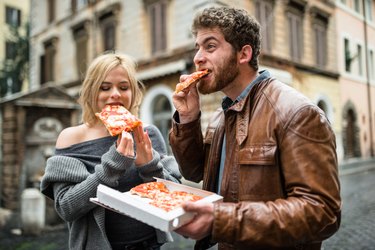 couple eating a pizza in italy not practicing how to how to eat healthy on vacation.