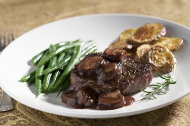 A white plate with a piece of steak with Mushroom Wine Sauce and Vegetables