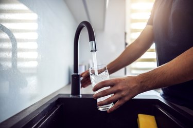 Close up of person's hand filling glass with water from kitchen sink