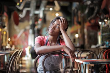 Tired bartender sitting on chair holder her head wondering, 