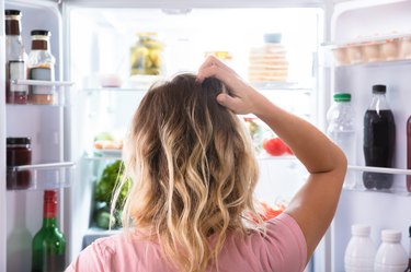 A woman who is eating too few calories on her diet is hungry and looking in the refrigerator