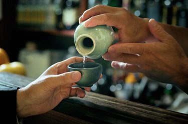 Close-up of bartender hand pouring Sake to glass which hands of adult man.