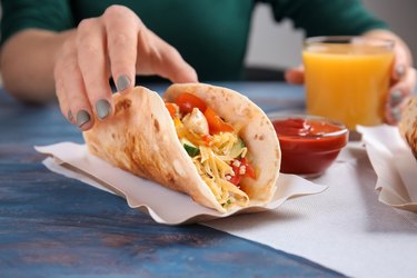 Woman eating tasty taco at table, closeup