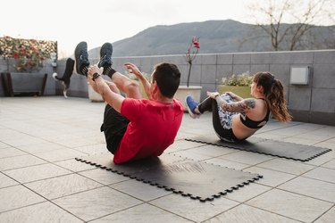 mature man and young woman Doing crunches with sportswear on the terrace of his house at sunset