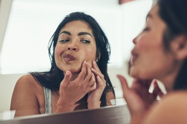 A woman looking at her skin in the mirror after a workout