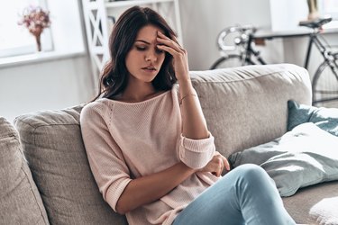 a person sits on a gray couch holding their head with a hunger headache