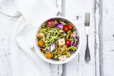 Bowl of zoodles with fried tofu, red quinoa, red onions and tomatoes