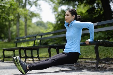 Person performing triceps dips outside on a park bench