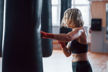 Full kickback. Female boxer is punching the bag. Blonde have exercise in the gym