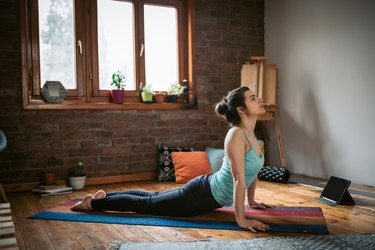 Person in blue tank top and black leggings doing an upward facing dog yoga pose at home to demonstrate core stretches for abs