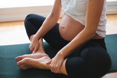 close up of pregnant person in butterfly stretch on teal yoga mat staying fit and toning up