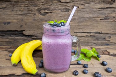 Blueberry and banana smoothie purple colorful fruit juice milkshake blend beverage healthy high protein the taste yummy In glass drink episode morning on a wooden background.