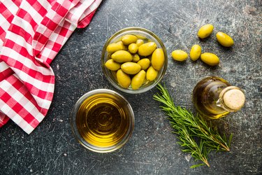Green olives and olive oil in glass bowl.