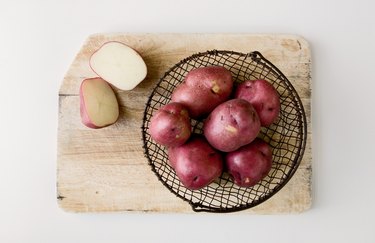 Red potatoes in wire basket on cutting board.