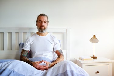 A mature man sitting in bed doing a 5 minute morning mediation to set his intentions for the day