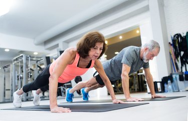 Senior couple in gym working out, doing push ups