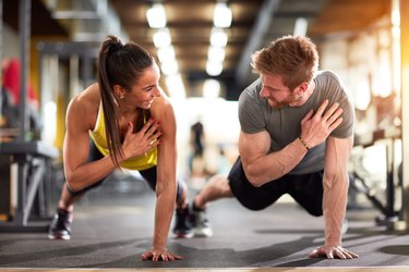 Fit man and woman doing push-ups and working out at the gym