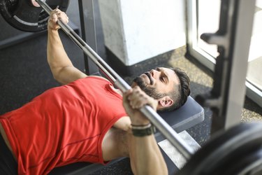 man in red tank top doing chest presses on a weight bench