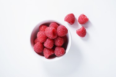 raspberries in white bowl on white background