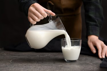 Woman pouring fresh milk from jug into glass on table
