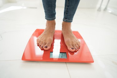 A woman's feet standing on a red scale in a white marble bathroom