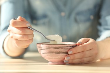 closeup of bowl with probiotic yogurt and spoon in female hands