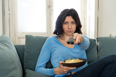 Young upset woman on sofa using control remote zapping bored of bad TV shows and programing . Looking disinterested, aloof and sleepless. People, too much bad television and Sedentary lifestyle.