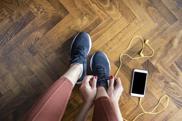 Woman tying shoelace before workout with smartphone and headphones